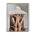 Framed artwork of a person wearing a large straw hat sitting on a chair.